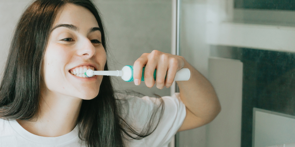 A girl brushing her teeth with an electric toothbrush to ensure she cares for her dental onlays