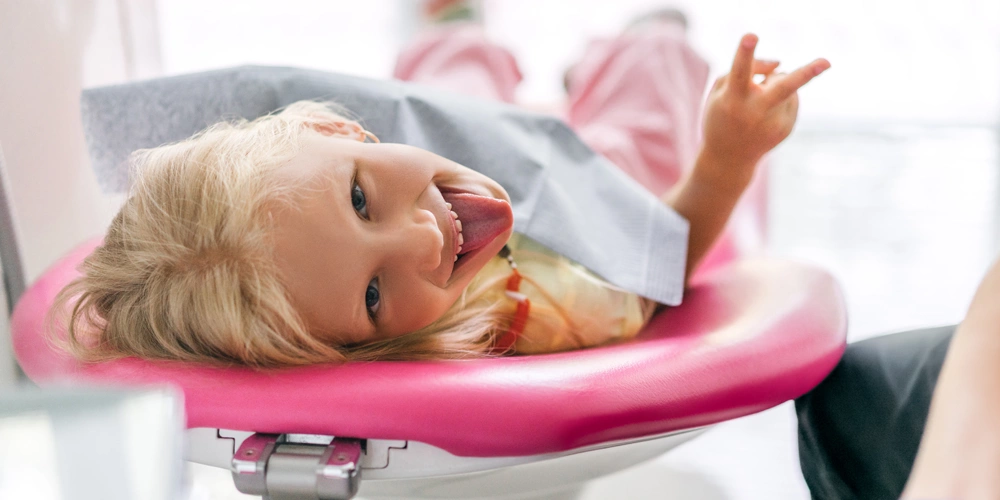 A young girl laying back in a dental chair smiling after getting dental sealants