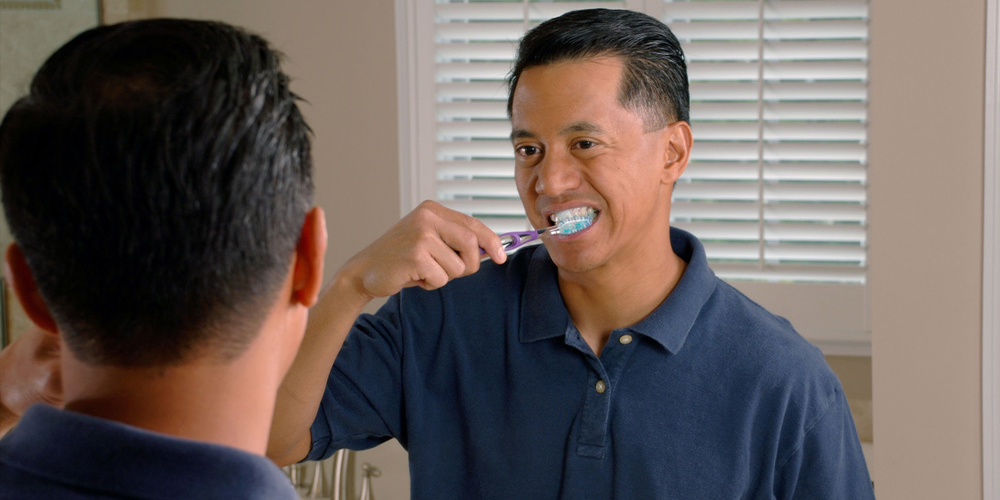 A man brushing his teeth in the mirror to ensure the life of his root canal therapy and the crown