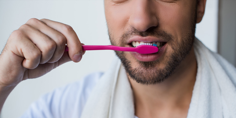 A man brushing his teeth to ensure he prolongs the life of his dental bridge