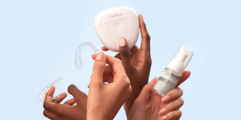 Multiple hands holding up at home teeth whitening trays, gels, and ultraviolet light