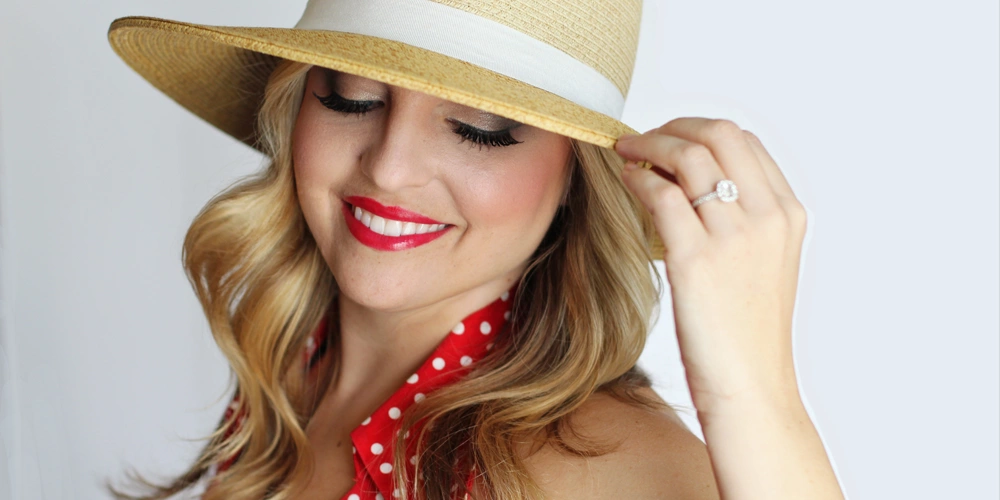A women with a hat smiling in a red dress with her porcelain dental crowns