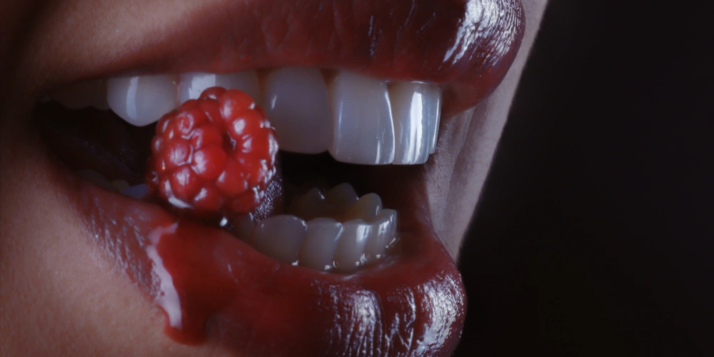 A women chewing on a raspberry showing premature tooth wear